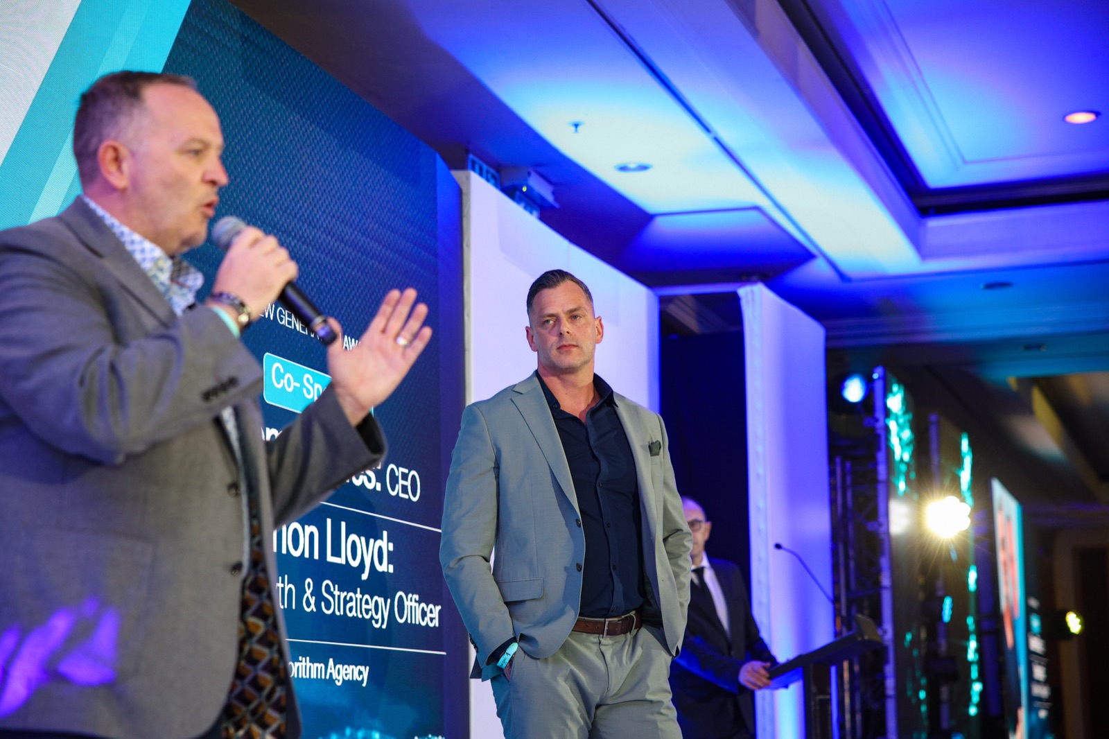 Graeme Stiles speaking from the New Generation Awards stage, with Algorithm Agency Chief Growth & Strategy Officer visible in the background.